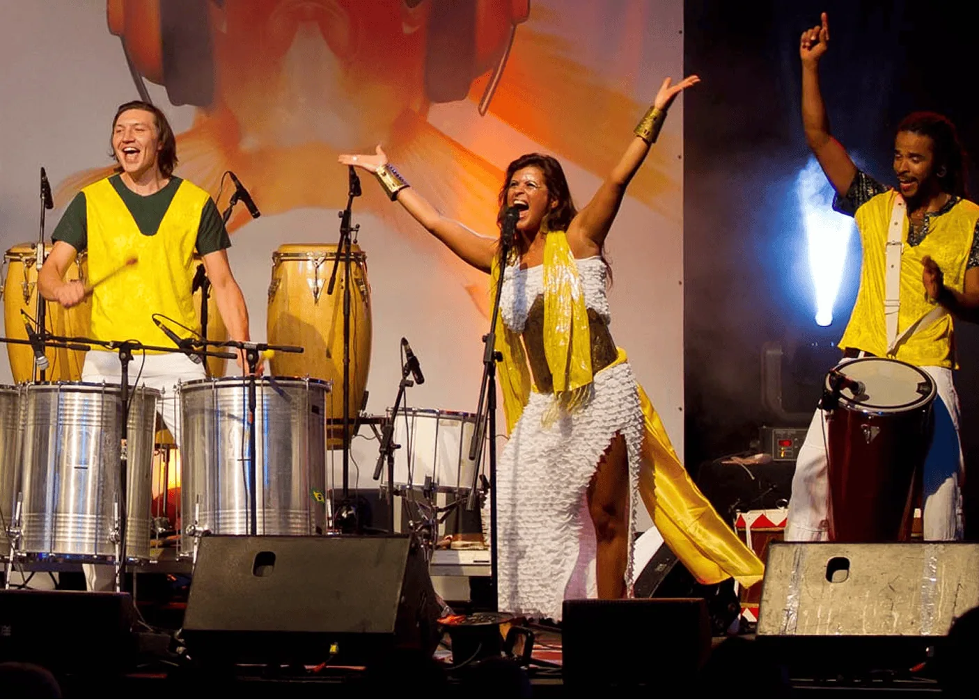 Musiker bei einer Live-Performance mit Trommeln und Gesang auf der Bühne, gekleidet in gelbe und weiße Kostüme.