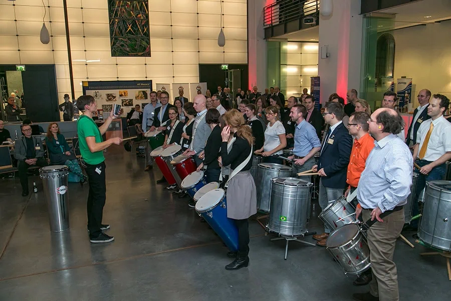 Gruppe von Personen, die an einem Samba-Team-Event mit Trommeln teilnehmen, geleitet von einem Instruktor.