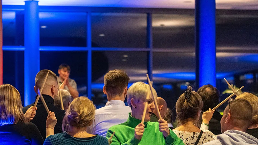 Teilnehmer eines Team-Events halten Schlagstöcke in einer beleuchteten Umgebung während einer Darbietung.