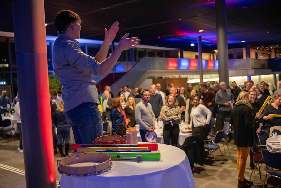 Person, die auf einer Bühne steht und mit Instrumenten eine musikalische Darbietung während eines Team-Events leitet.