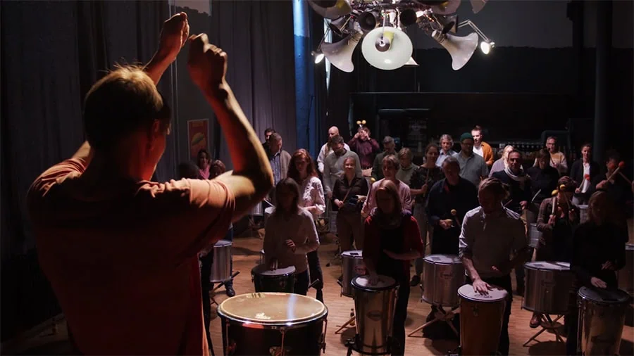 Gruppe von Personen, die an einem Team-Event mit Trommeln und einem Dirigenten teilnehmen.