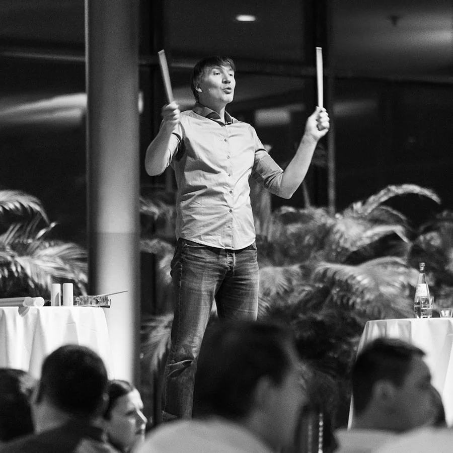 Tino Vetter, der mit zwei Stöcken dirigiert, steht auf einer erhöhten Fläche bei einer Veranstaltung.