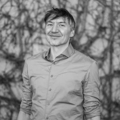 Porträt eines Mannes mit kurzen Haaren und einem lächelnden Gesicht, der ein graues Hemd trägt.